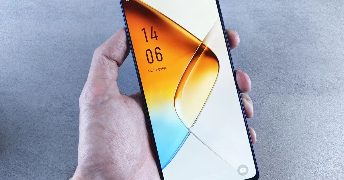 Vue rapprochée d'une main tenant un smartphone élégant avec un écran d'accueil sur le thème orange, mettant en valeur la technologie moderne.