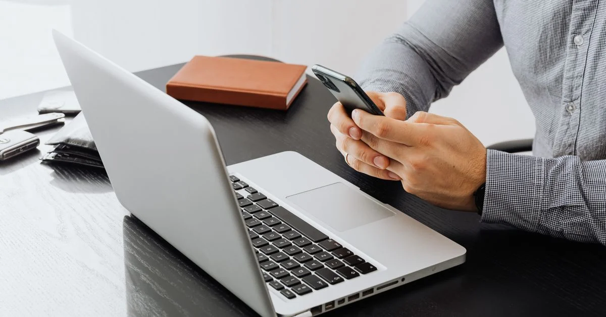 Un adulte utilisant un smartphone à un bureau avec un ordinateur portable pour le travail.