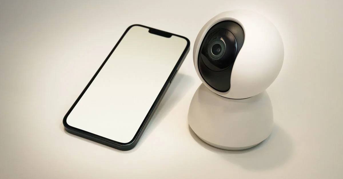 Une caméra de sécurité moderne pour maison intelligente à côté d'un smartphone à écran vide, mettant en avant la technologie d'automatisation de la maison.